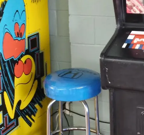 Blue Honda stool between the arcade cabinets